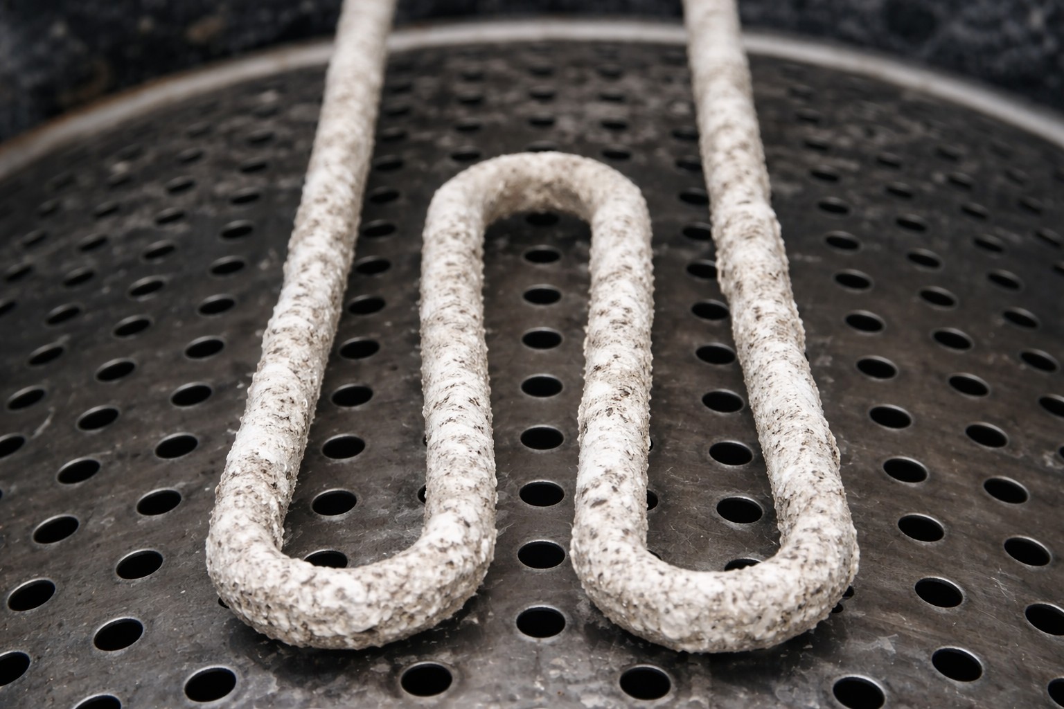 Verroest verwarmingselement met kalkaanslag op geperforeerd metalen oppervlak.