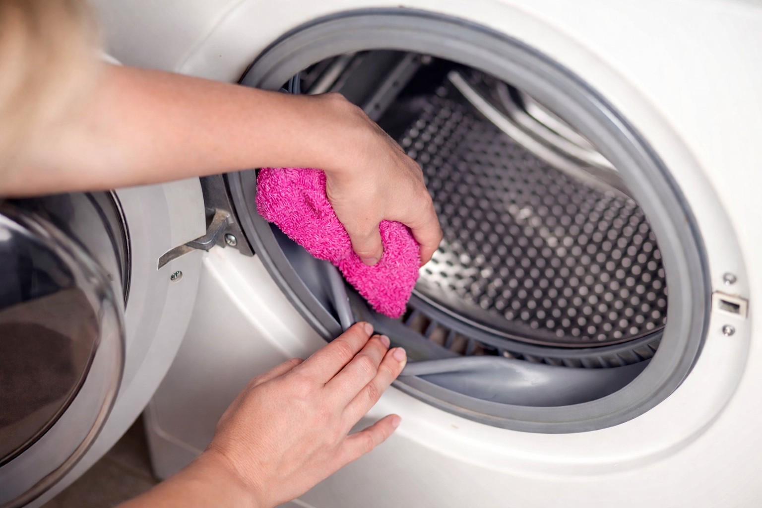 Iemand maakt de binnenkant van een witte wasdroger schoon met een roze doek.